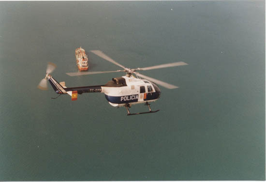 Helicóptero de Policía Nacional sobrevolando el mar por el que navega un carguero, realizando labores de apoyo en control marítimo.