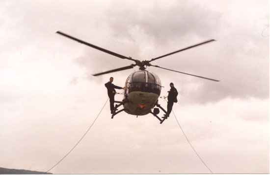 Helicóptero de Policía Nacional en vuelo de poca altura con dos miembros de Unidades Especiales en el exterior, preparados con cuerdas de rapel.