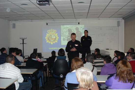 Un policía de la Unidad Central de Participación Ciudadana y Programas, dando una charla a padres y alumnos en un aula, junto con una policía.