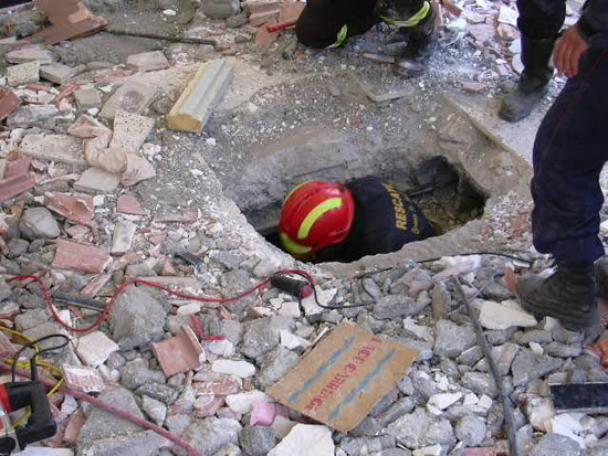 Miembro de un equipo de rescate se introduce en agujero, alrededor se pueden observar multitud de escombros.