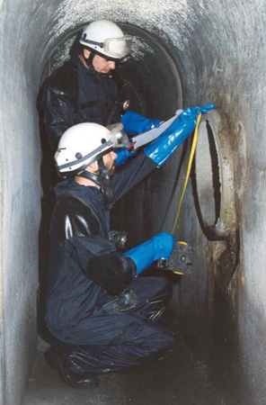 Policías Nacionales de la Unidad de Subsuelo y Protección Ambiental equipados con mono de trabajo realizando una inspección de una alcantarilla.