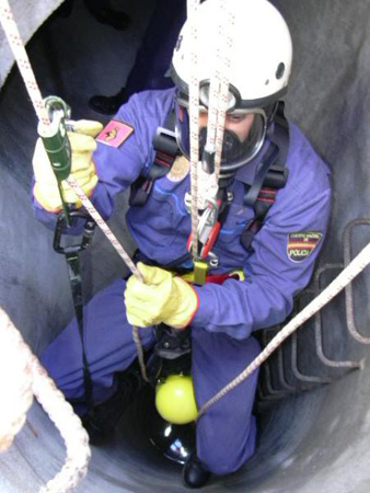 Policía Nacional de la Unidad de Subsuelo y Protección Ambiental equipado con un mono de protección, bajando por un pozo ayudado de una cuerda.