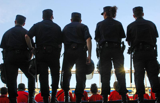 Cinco miembros de la Unidad de Intervención Policial, cuatro hombres y una mujer, vigilando en un estadio durante la celebración de un partido.