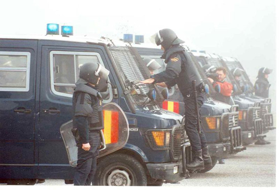 Cuatro furgones antiguos en formación tipo en línea. Un policía colocando la protección del cristal delantero del furgón. Otros en formación.