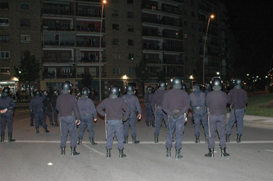 Más de quince policías en formación vigilando el desarrollo de una manifestación. Es de noche. Portan el casco en protección, sobre la cabeza.