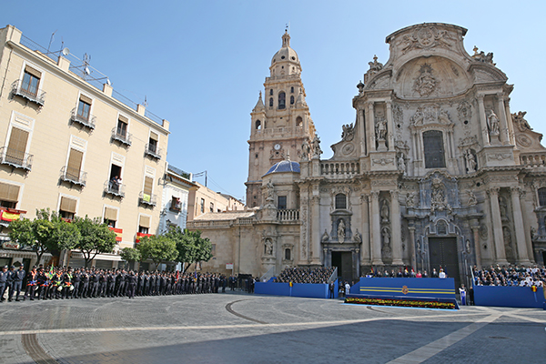 Plaza de la Catedral de Murcia. Frente a la puerta  el palco de autoridades. A la izquierda policías en formación. Balcones con banderas de España.