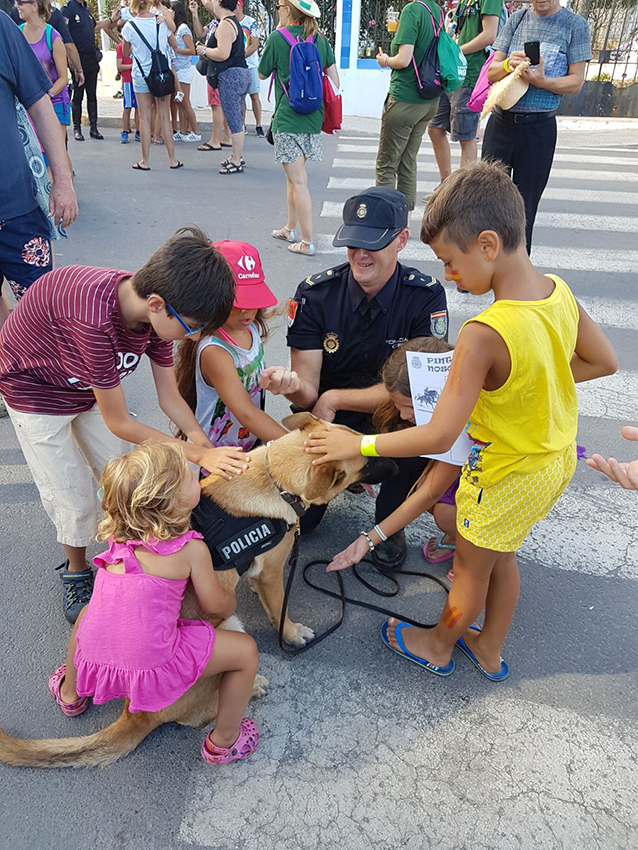 Niños acariciando a un perro policía que está junto a su compañero de la unidad de guías caninos