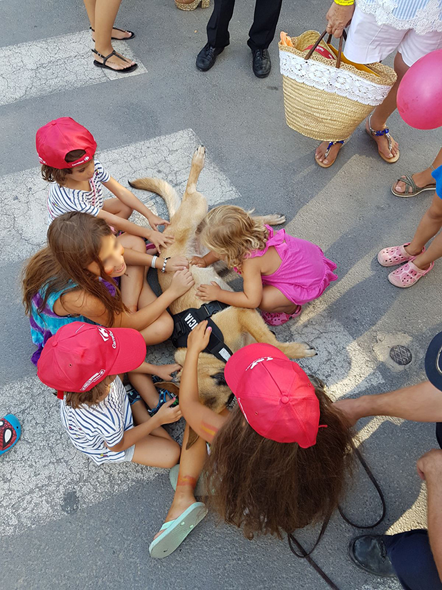 Niños acariciando a un perro policía que está tumbado en el suelo
