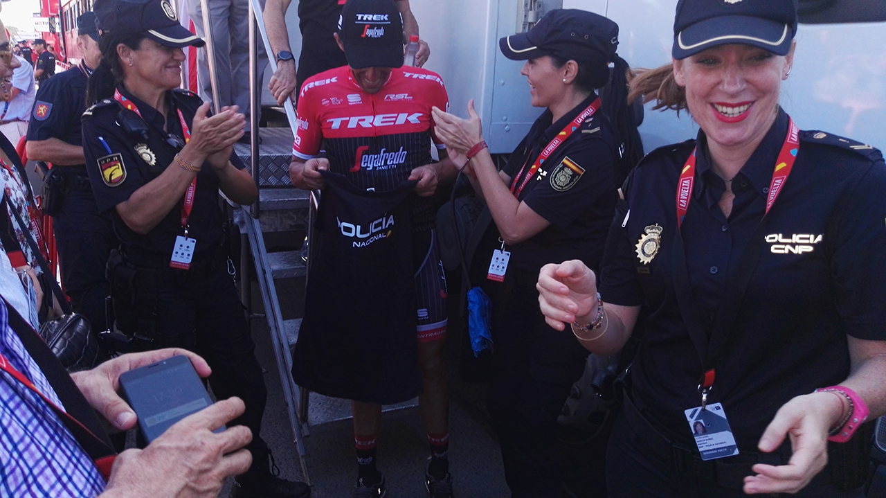 Tres mujeres policías con Alberto Contador,  al que están aplaudiendo y le han entregado una camiseta de policía