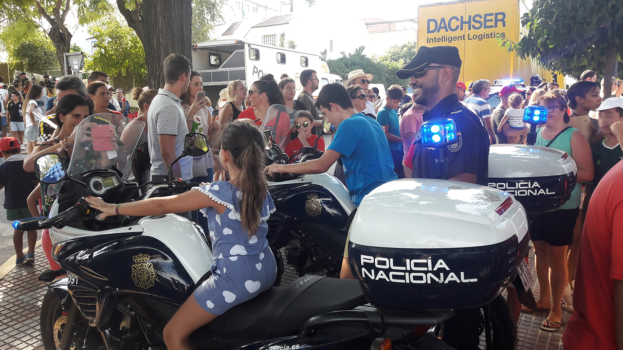 Niños montados en motocicletas policiales bajo la supervisión de un agente y numeroso público viendo los vehículos policiales