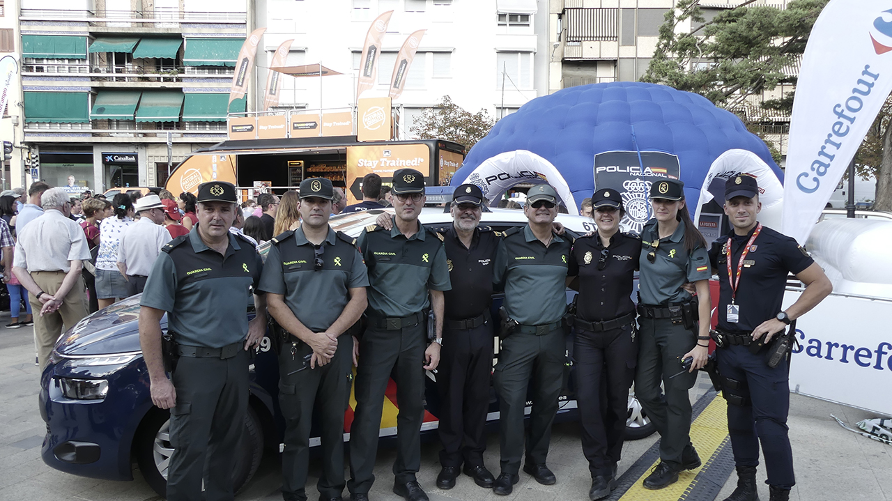 Agentes de la Guardia Civil y de Policía Nacional, posando delante de un vehículo policial y detrás la carpa informativa