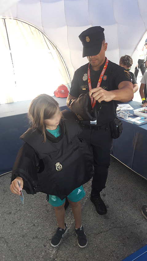 Un agente de policía ayudando a un niño a ponerse un chaleco policial, están dentro de la carpa informativa