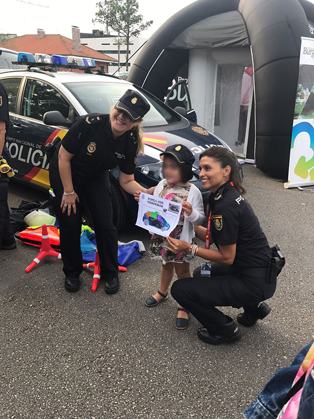 Dos agentes de policía posando con una niña que muestra el dibujo que ha hecho