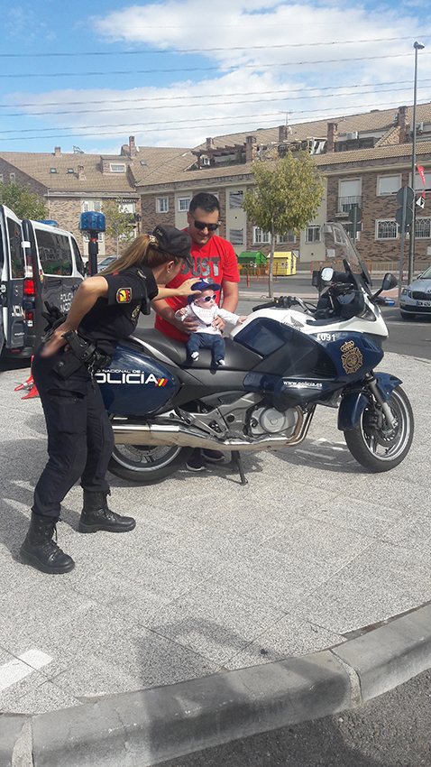 Un hombre sujetando a un bebé sobre motocicleta policial y agente de policía colocando la gorra reglamentaria 