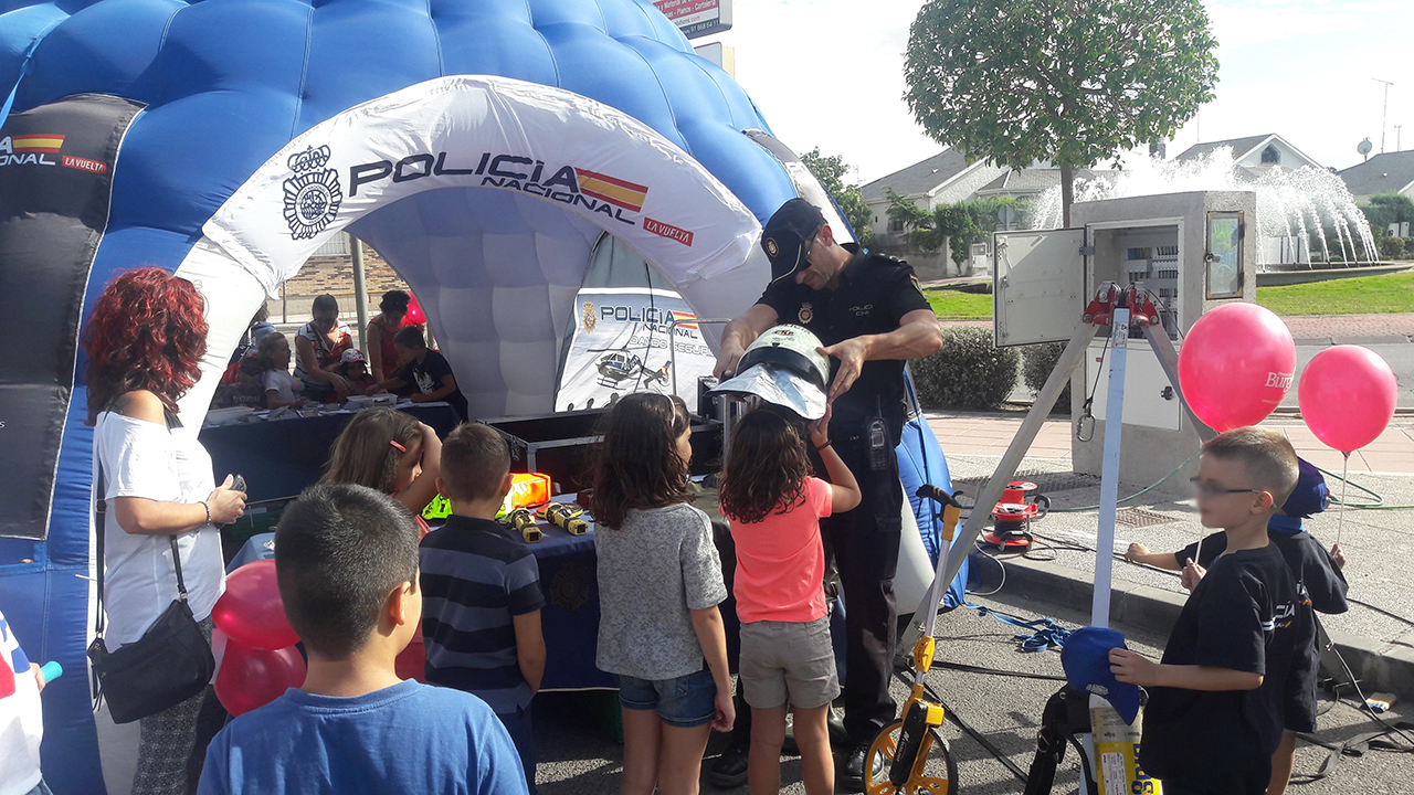 Agente de policía colocando a una niña un casco, delante de la carpa informativa, junto con otros niños que están mirando