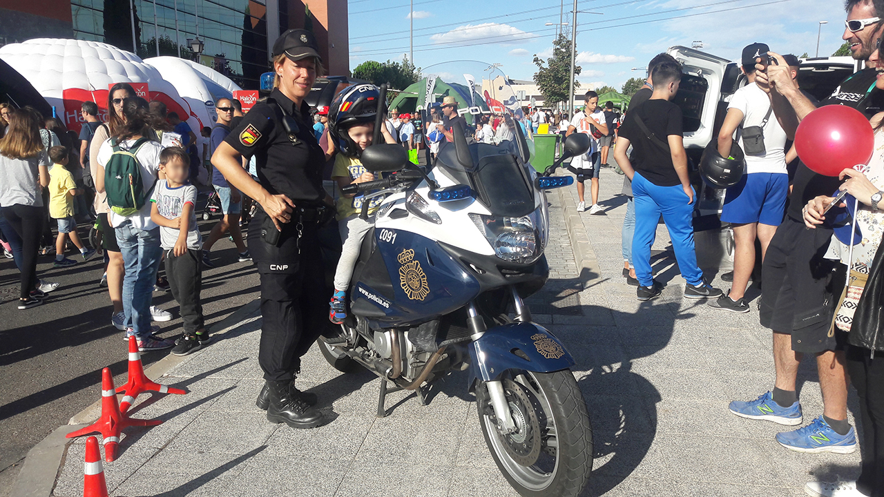 Una agente de policía posando para foto con un niño montado en una motocicleta y llevando un casco de policía