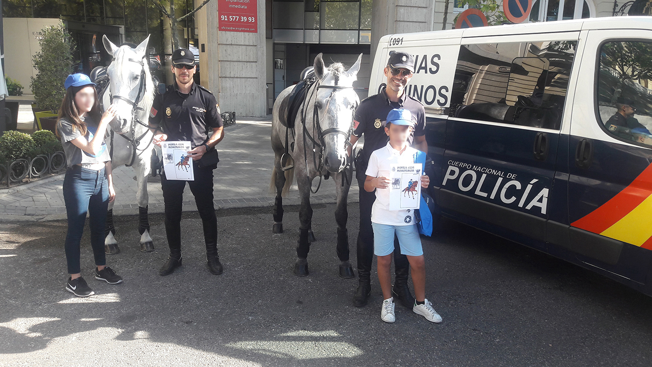 Dos policías de la unidad de caballería junto a sus caballos y dos niños que muestran sus dibujos