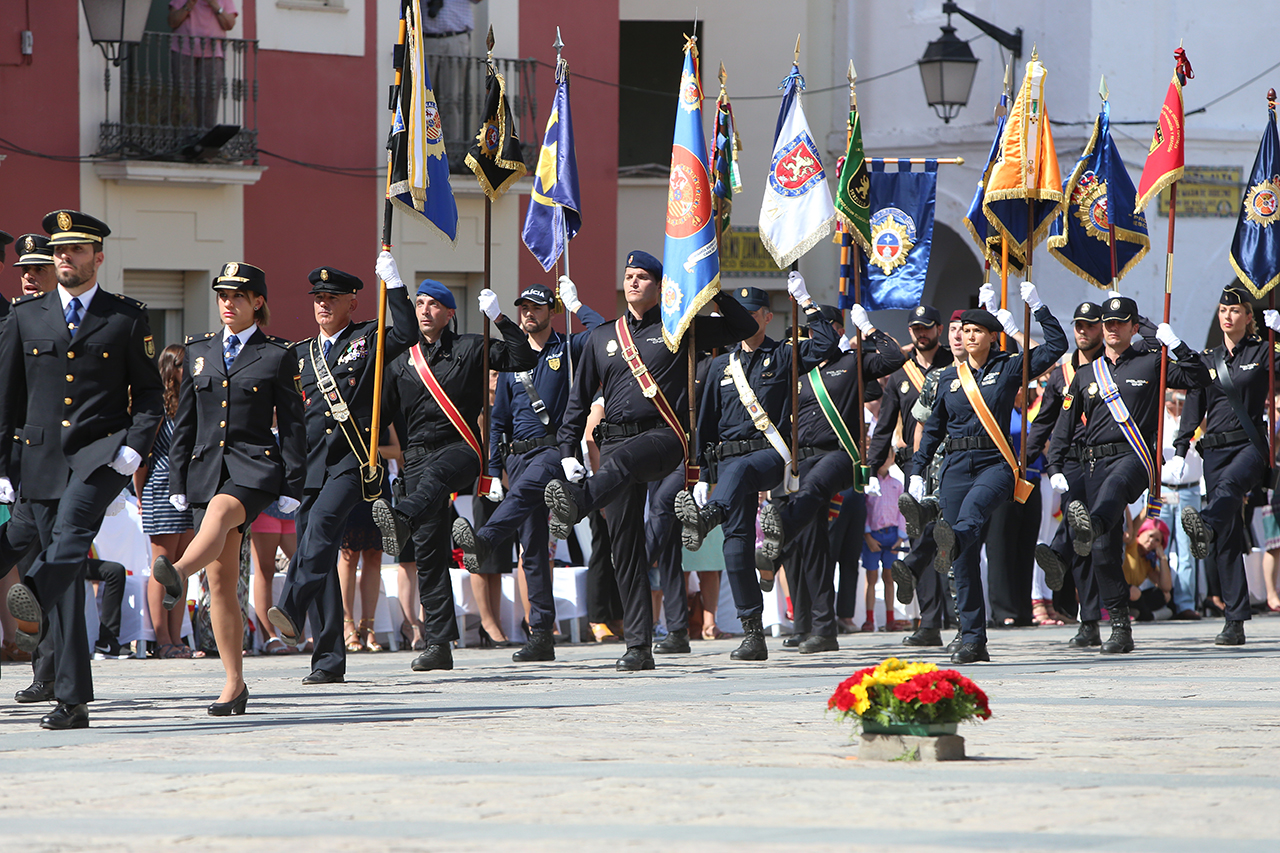 Desfile de policías uniformados de distintos cuerpos portando las banderas distintivas. 