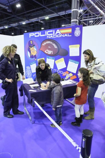 Policía haciendo una demostración a un niño de como se toman las huellas. Hay otros dos policías, una señora y una niña.