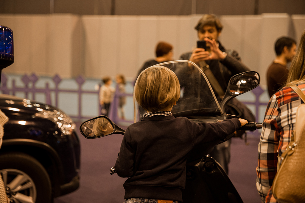 Niño de espaldas, subido en una motocicleta, posando, frente a él un  adulto con el móvil realizando una foto.