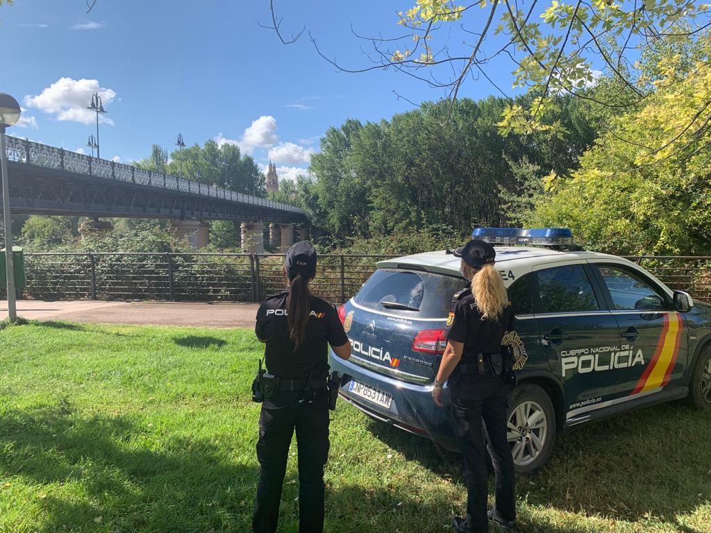 Dos mujeres policía junto a un coche policial observando un puente.