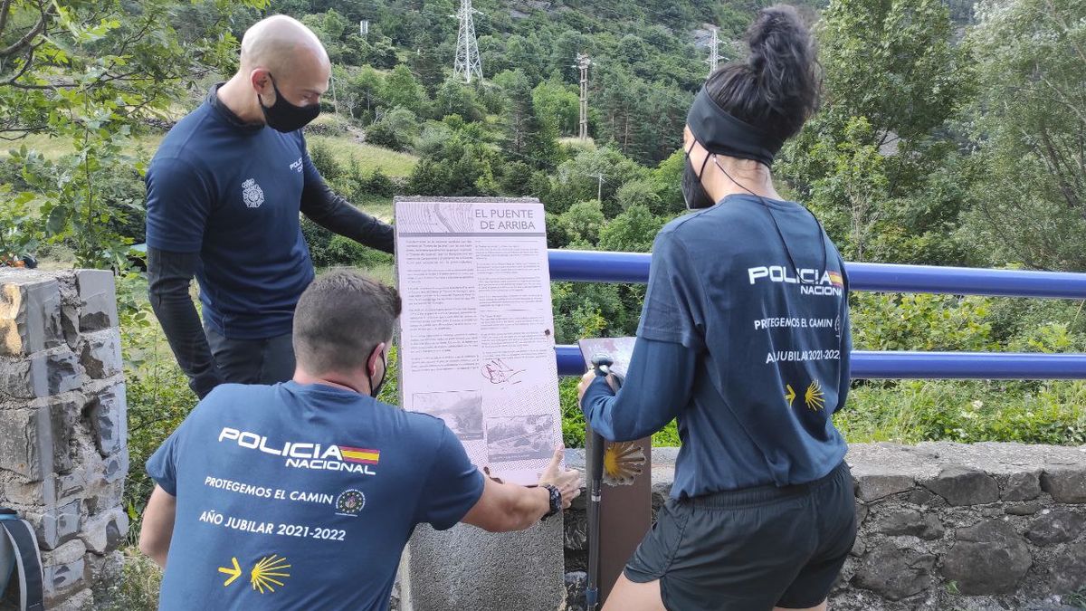 Dos hombres y una mujer vistiendo la camiseta oficial de Protegemos el Camino, leyendo una placa informativa en El Puente de Arriba