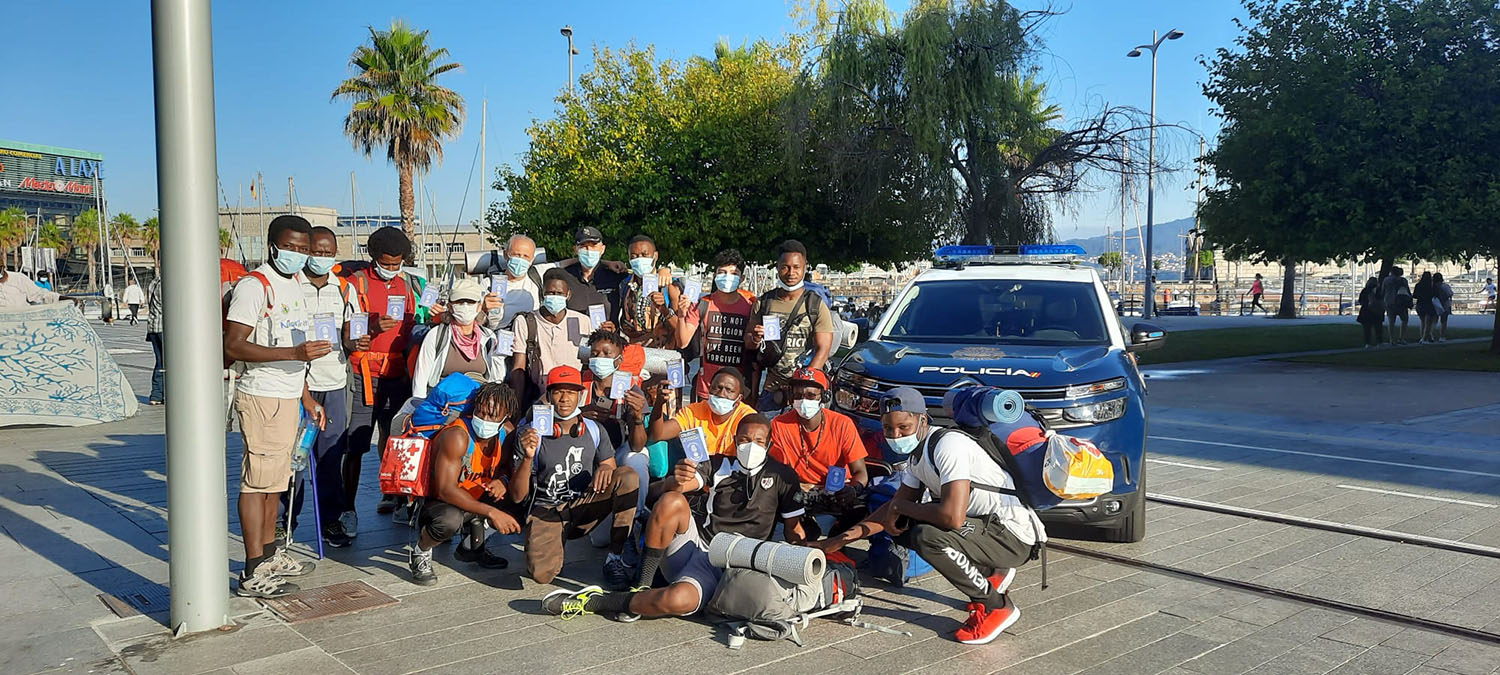 Un grupo numeroso de peregrinos posando para la foto junto con un policía y un coche policial, mostrando la cartilla del peregrino de Policía Nacional
