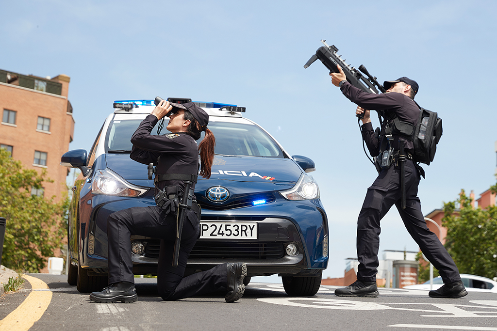 Hombre y mujer uniformados de la Policía Nacional. Él con dispositivo anti-dron. Ella con prismáticos.