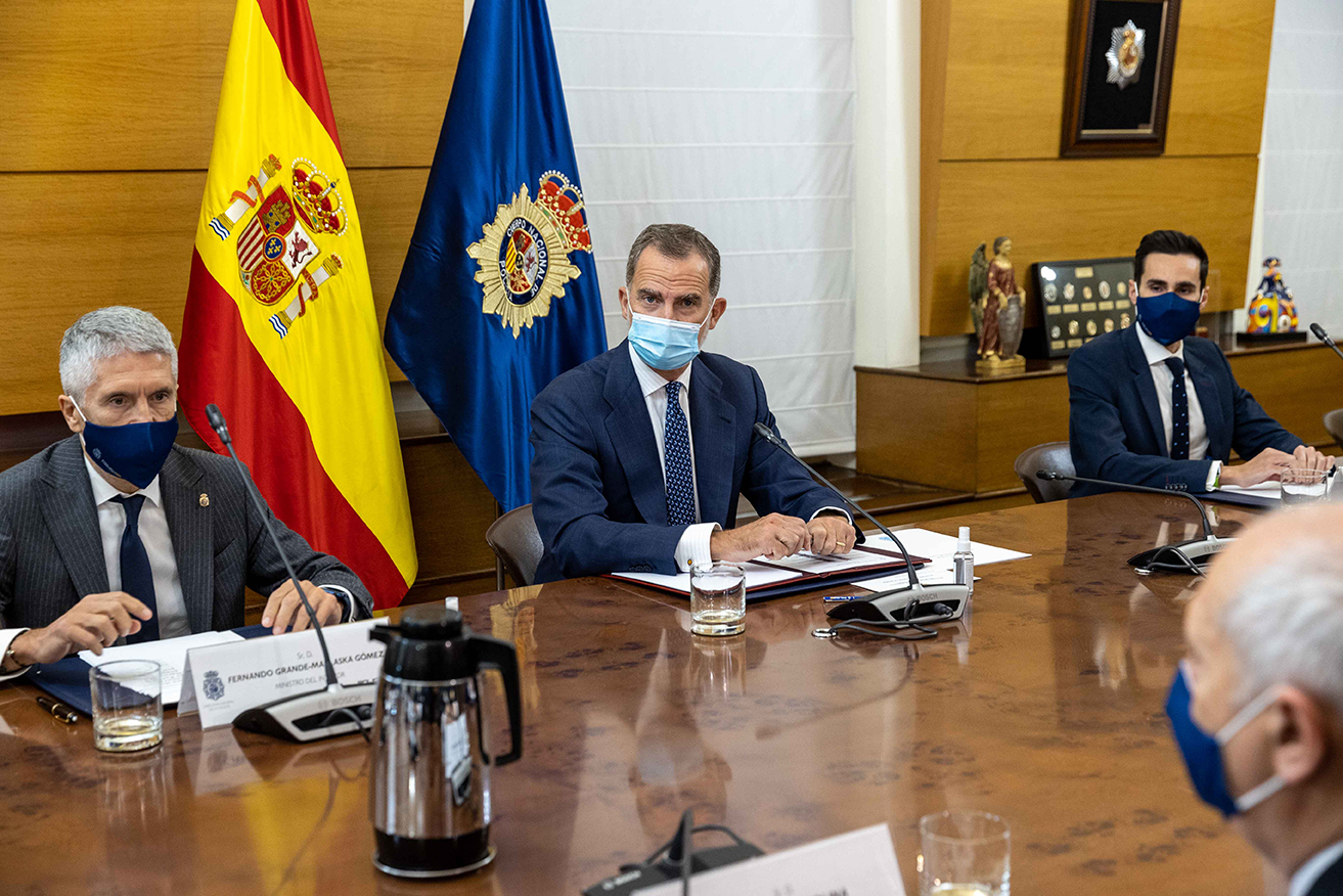 S.M. el Rey, a su derecha el Ministro del Interior y a su izquierda el Secretario de Estado de Seguridad sentados en la mesa de la sala de reuniones.