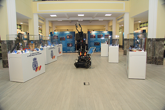Sala de exposición con varias vitrinas con material y un robot de desactivación de explosivos en el centro.
