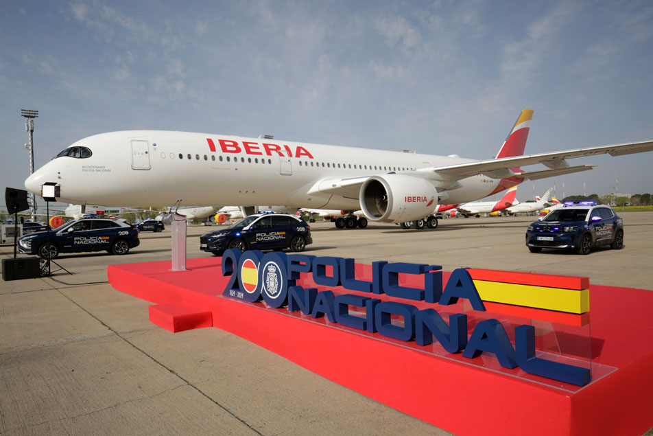 Avión de Iberia junto a rótulo conmemorativo del bicentenario de la Policía Española y vehículos policiales.