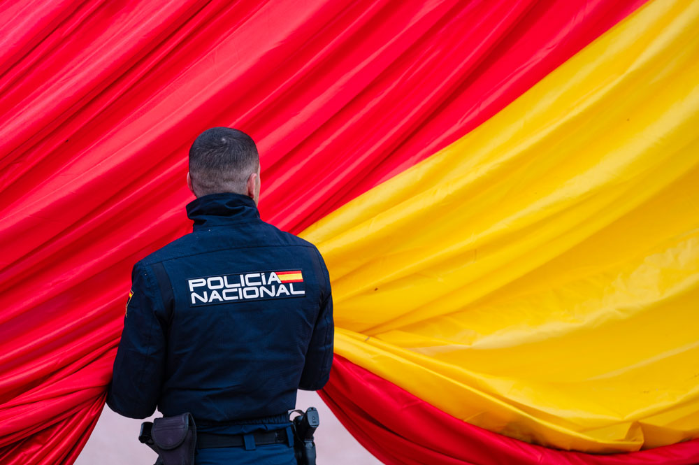 Policía Nacional de espalda sujetando la Bandera de España.