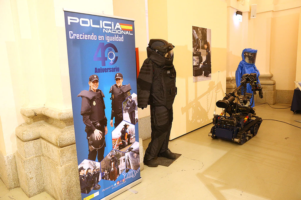 Sala con cartel del aniversario, uniformes y robot para la desactivación de explosivos. En la pared cartel mostrando a mujer policía manejando robot.