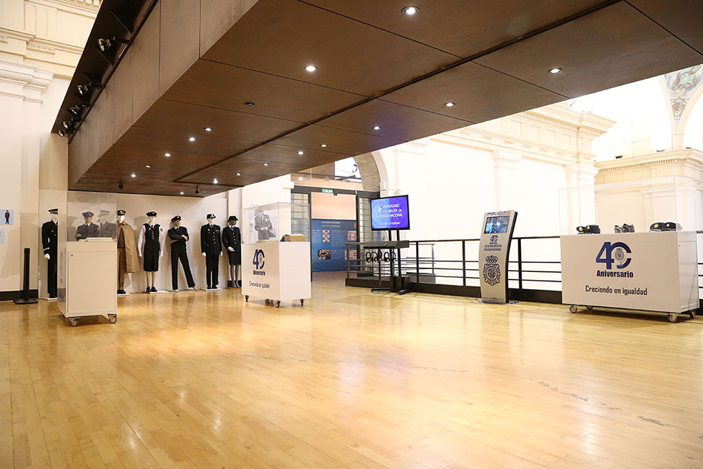Sala de exposición con distintos uniformes policiales, tres vitrinas exponiendo gorras y efectos policiales, una pantalla y un kiosco interactivo.