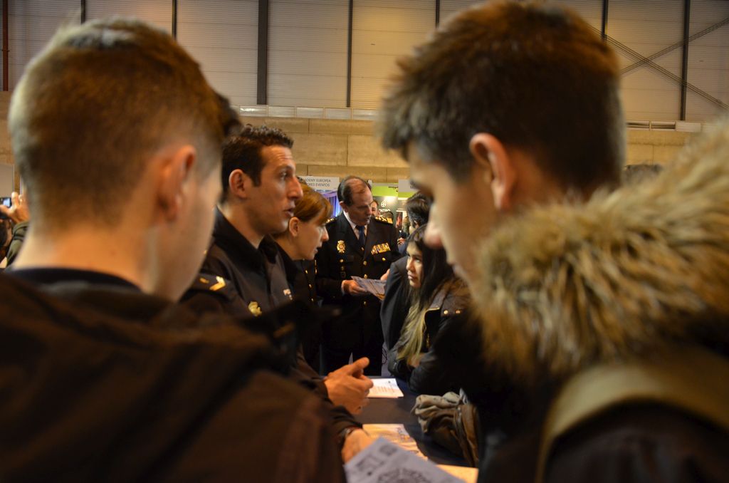 Dos chicos jóvenes viendo tríptico con información. Al fondo,  miembros de la Policía Nacional informando a otros jóvenes.