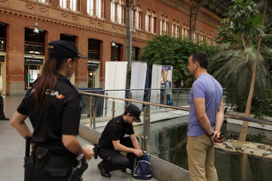 Junto al estanque de la estación de Atocha (Madrid), un policía registra la mochila de un ciudadano mientras una policía lo vigila. 