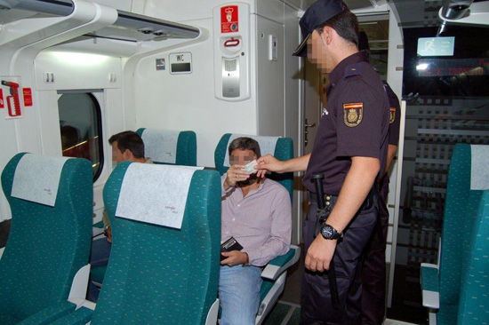 Dos policías Nacionales realizan un control de documentación a un ciudadano sentado en el asiento de un tren.